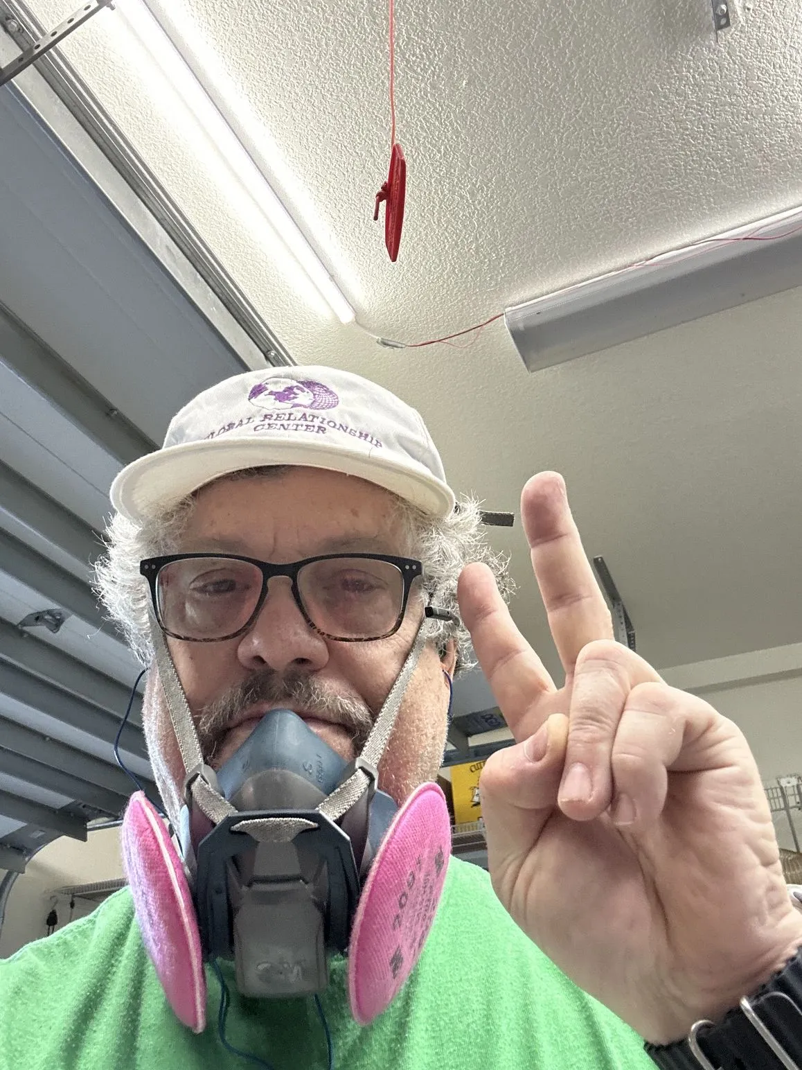 David in the workshop in a respirator, flashing a peace sign.