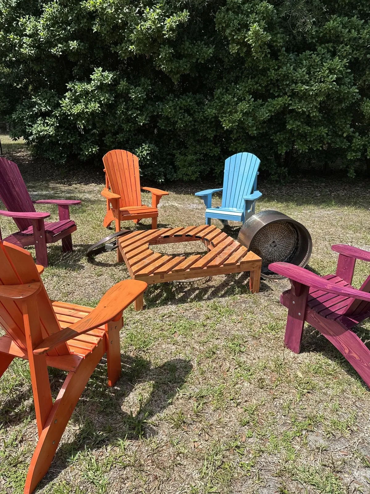 A ring of brightly painted Adirondack chairs around a fire pit.