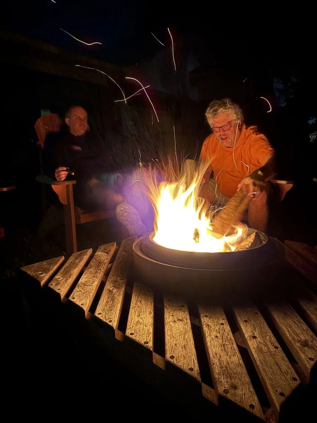 Gathered around a fire pit at night, sparks rising.